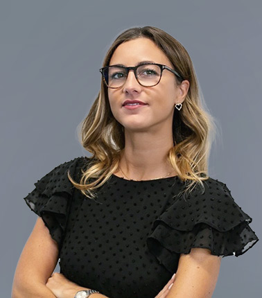 Donna con abito nero e capelli ondulati, indossa occhiali e orecchini a cuore.