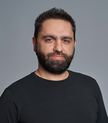 Uomo con barba e maglietta nera su sfondo grigio.