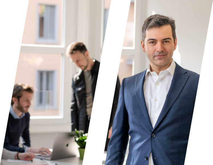 Uomo in abito blu professionale e due uomini al lavoro su un computer portatile in ufficio luminoso.