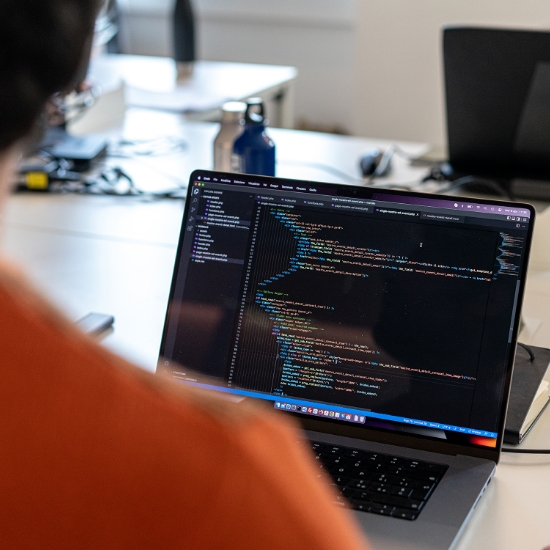 Persona che lavora su un laptop con codice aperto nell'editor su una scrivania.