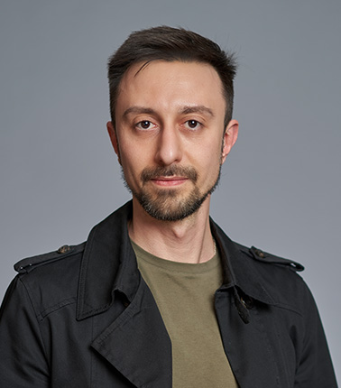 Giovane uomo con giacca scura e maglietta verde su sfondo grigio.