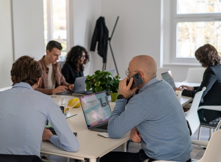 Gruppo di persone in un ufficio moderno, con laptop e un uomo che parla al telefono.