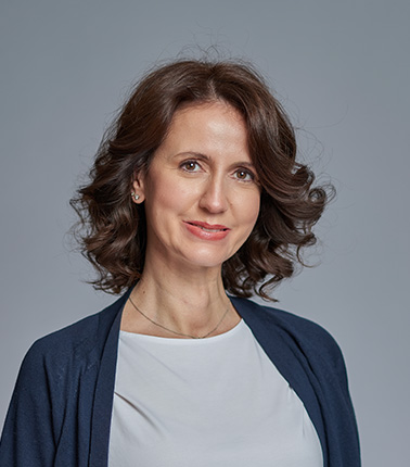 Donna con capelli castani e cardigan blu su sfondo grigio chiaro.