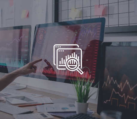 Postazione di lavoro con monitor che mostrano grafici finanziari e una mano che indica lo schermo.