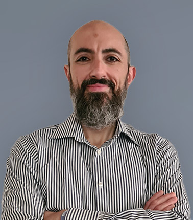 Uomo con barba e camicia a righe su sfondo grigio.